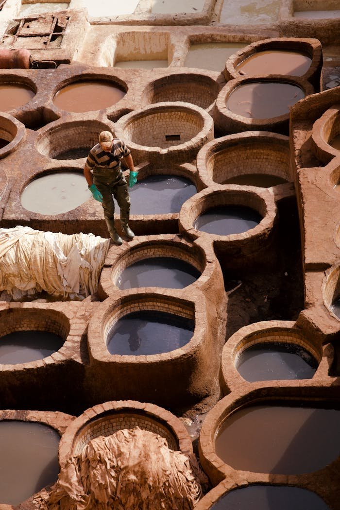 Man working in traditional Moroccan tannery pits, showcasing the leather tanning process.