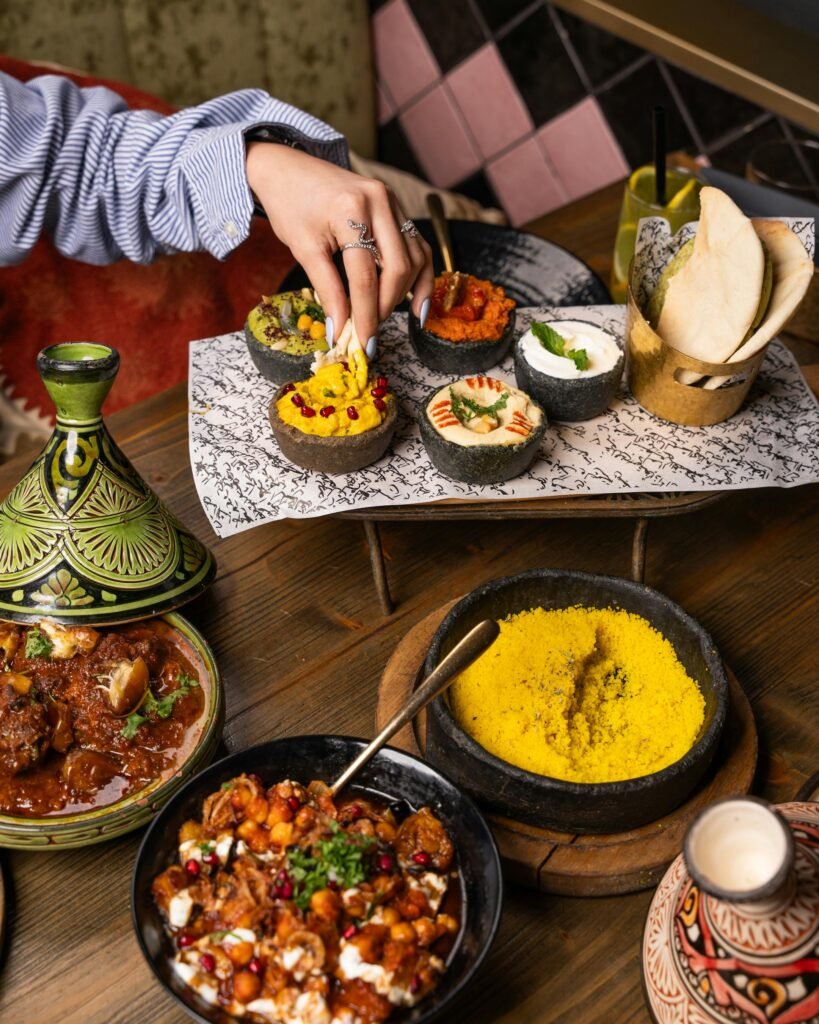 Home A vibrant Moroccan meal featuring beef tagine, various dips, bread, and yellow couscous, perfect for a cultural culinary experience.